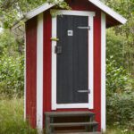 A red and white outhouse with steps leading to it.