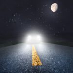 A car driving down the road at night with moon in background.