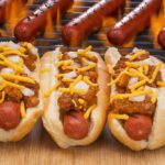 Three hot dogs with toppings on a grill.