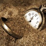 A broken pocket watch laying in the sand.