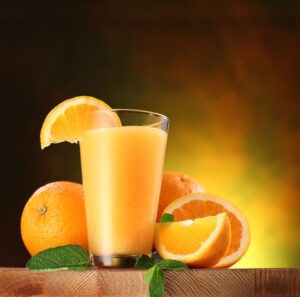 A glass of orange juice with some slices on the side