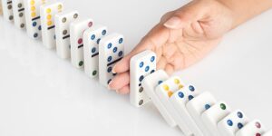 A hand is pushing the domino to stop it.