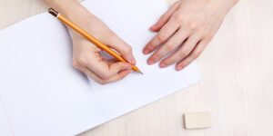 A person writing on paper with a pencil.