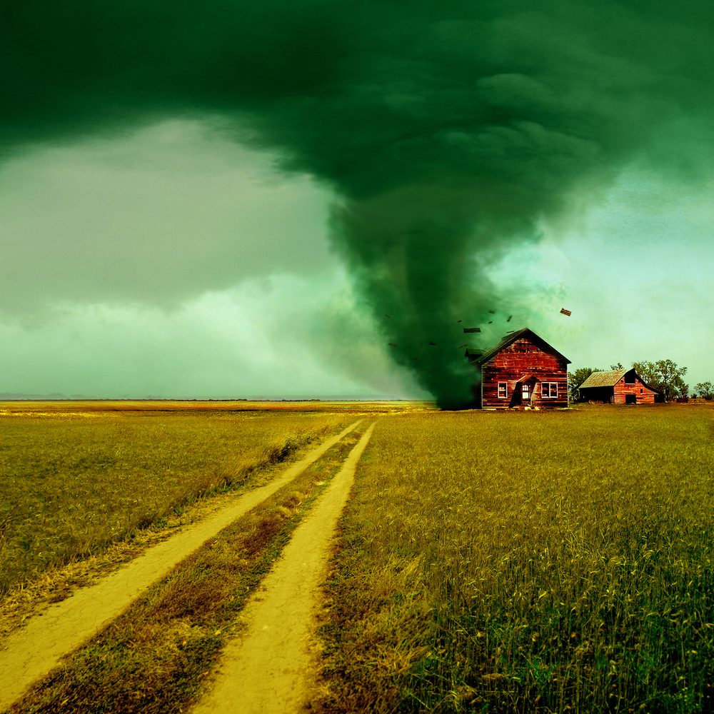 A red barn in the middle of nowhere with a tornado coming from it.
