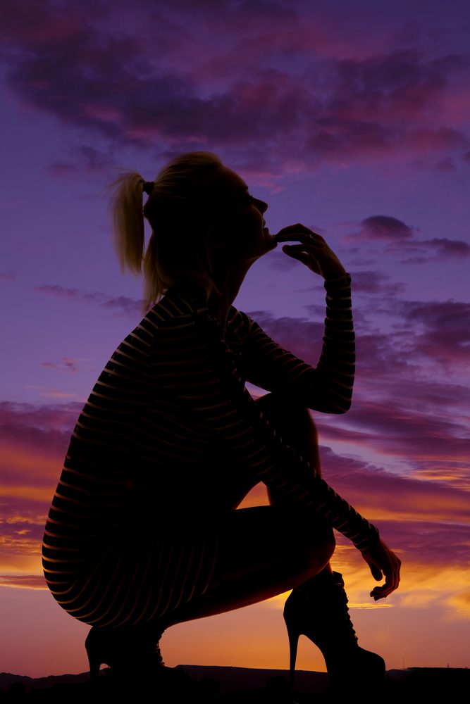 A woman sitting on the ground in front of a sunset.