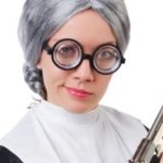 A woman with glasses and grey hair holding a gun.
