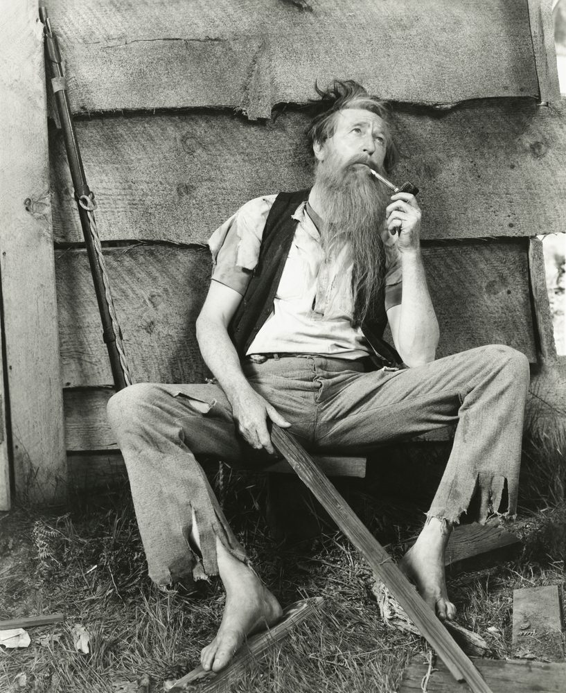 A man sitting on the ground with a beard and pipe.