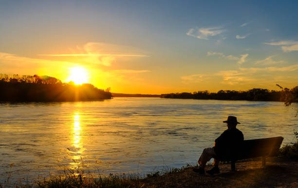 Senior man watching sunset on the Missouri River while sitting on a bench