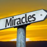 Sign pointing towards miracles at sunset