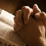 Hands clasped in prayer over a Bible