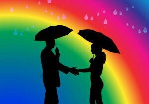 Two people holding umbrellas in front of a rainbow.