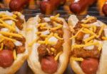 Three hot dogs with toppings on a grill.