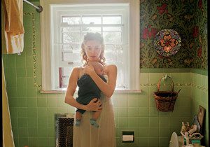 A woman in a bathroom holding a bottle.