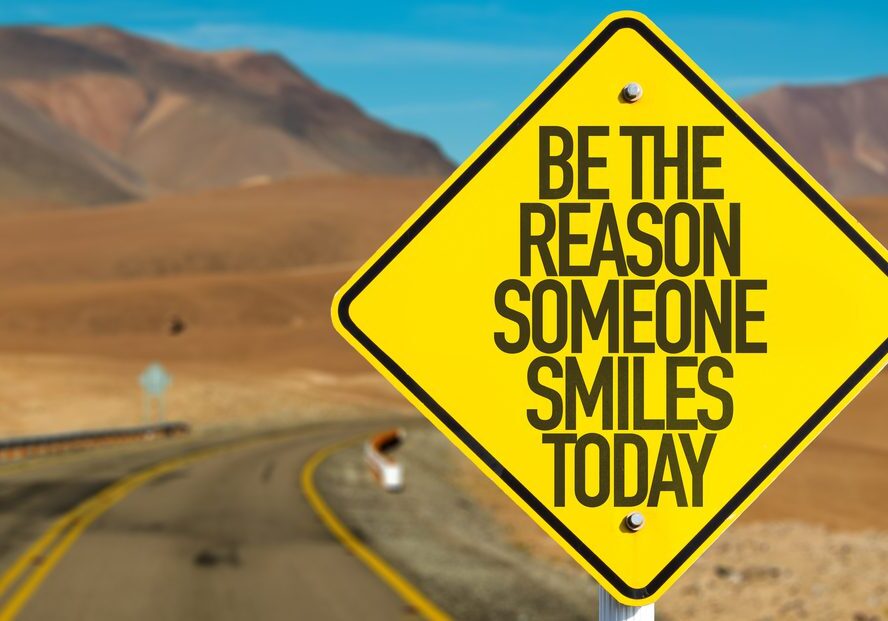 A yellow sign that says be the reason someone smiles today.