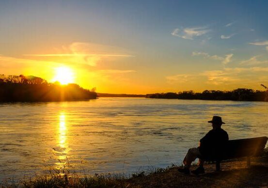 Senior man watching sunset on the Missouri River while sitting on a bench