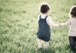 Two children holding hands in a field of grass
