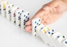 A hand is pushing the domino to stop it.